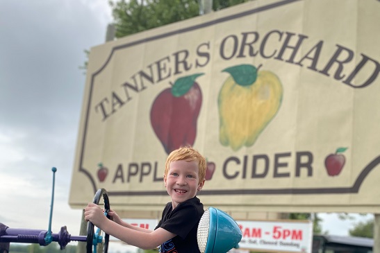 A child stands by the Tanners Orchard sign, which is an Apple Orchard for Aurora IL residents