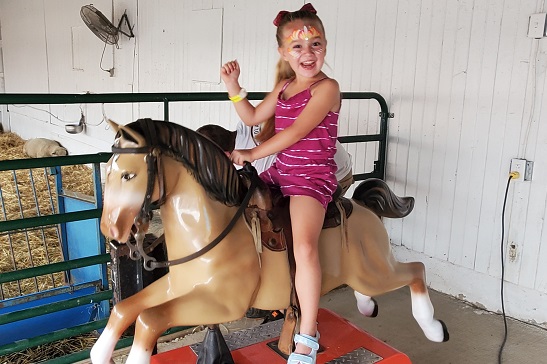 A girl with her face painted rides a coin-operated horse at Tanners Orchard, which offers Fall Activities for Aurora IL residents