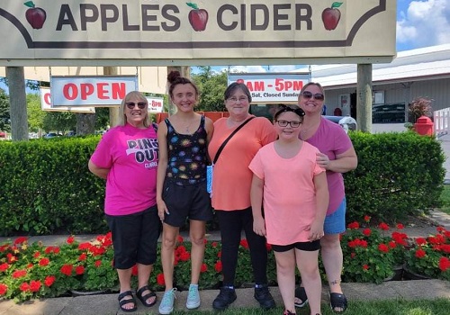 A family smiles in front of the Tanners Orchard sign. At Tanners, we are an apple orchard Dunlap IL families will love.