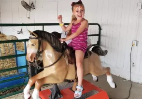 A girl with a painted face smiles while riding a motorized horse at Tanners Orchard, which offers one of the Best Ways to Celebrate Your Child's Birthday.