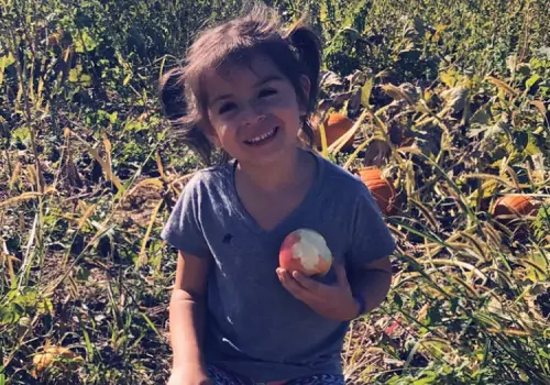 A girl holds an apple and smiles at Tanners Orchard, an Apple Picking Farm for Champaign IL residents