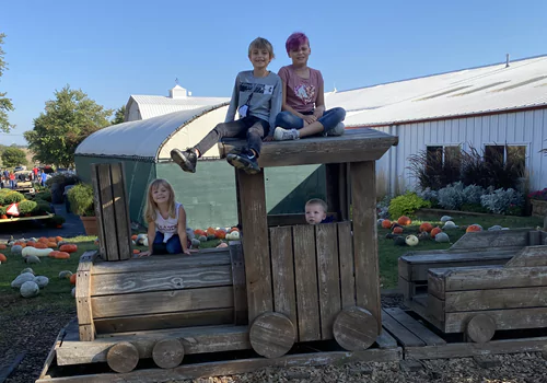 Kids pose on a wooden train at Tanners Orchard, which offers numerous Kids Activities for Aurora IL residents
